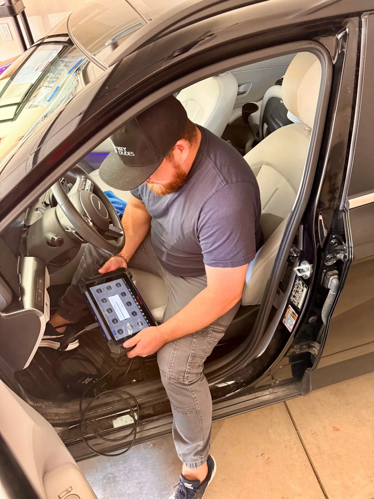 Garrett seated in a car with the door open, holding the key-programming tablet cabled to the car.